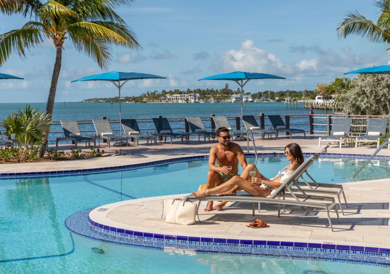A couple sitting by the pool on chaise lounges.