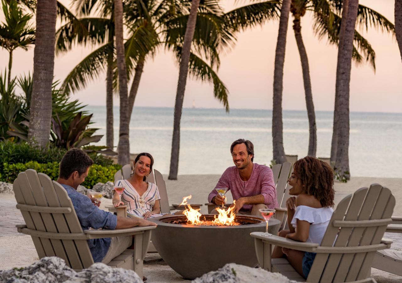 A group of people sitting around a fire by the ocean at Amara Cay Resort in the Florida Keys.