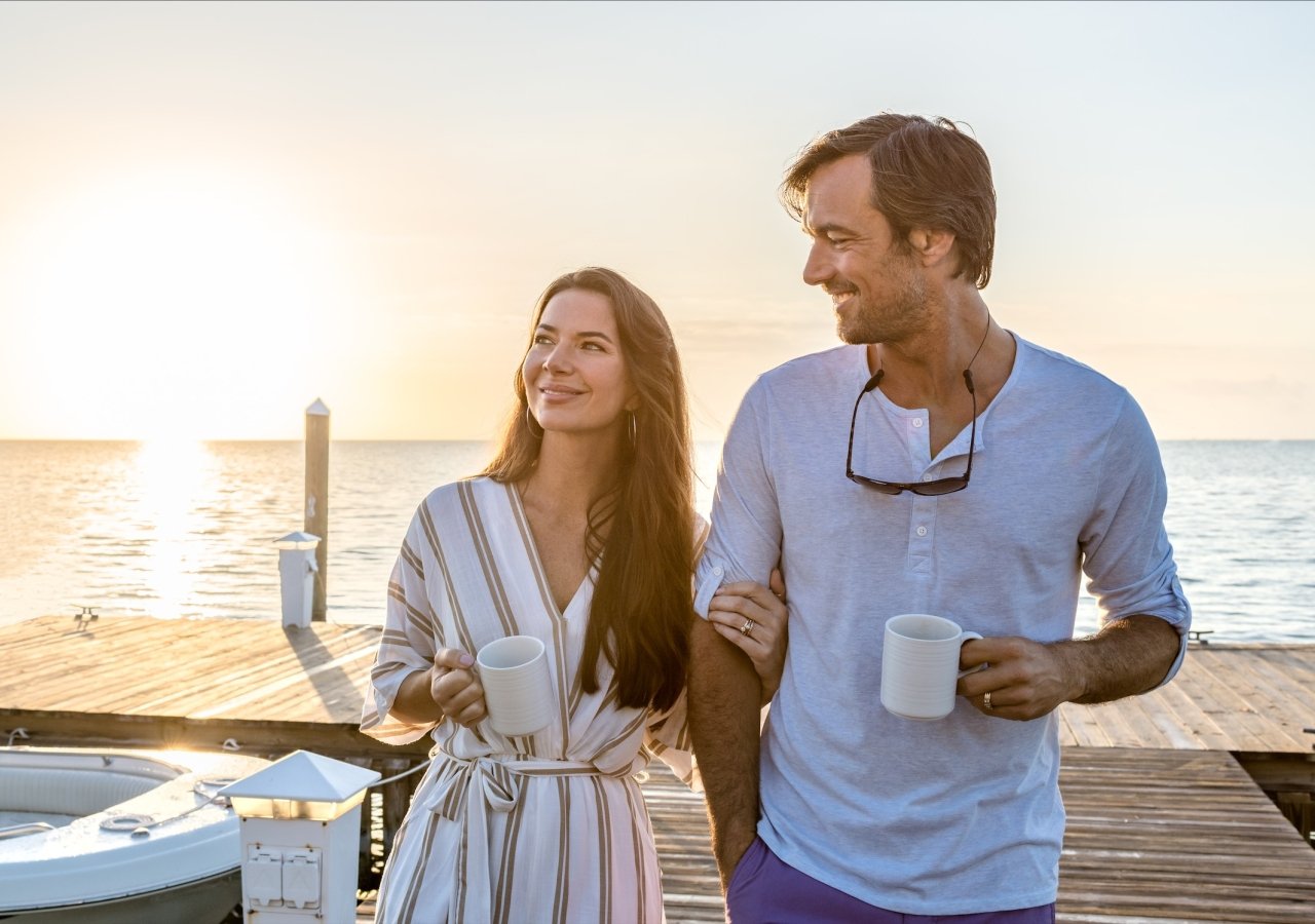 couple drinking coffee walking on a dock at sunrise