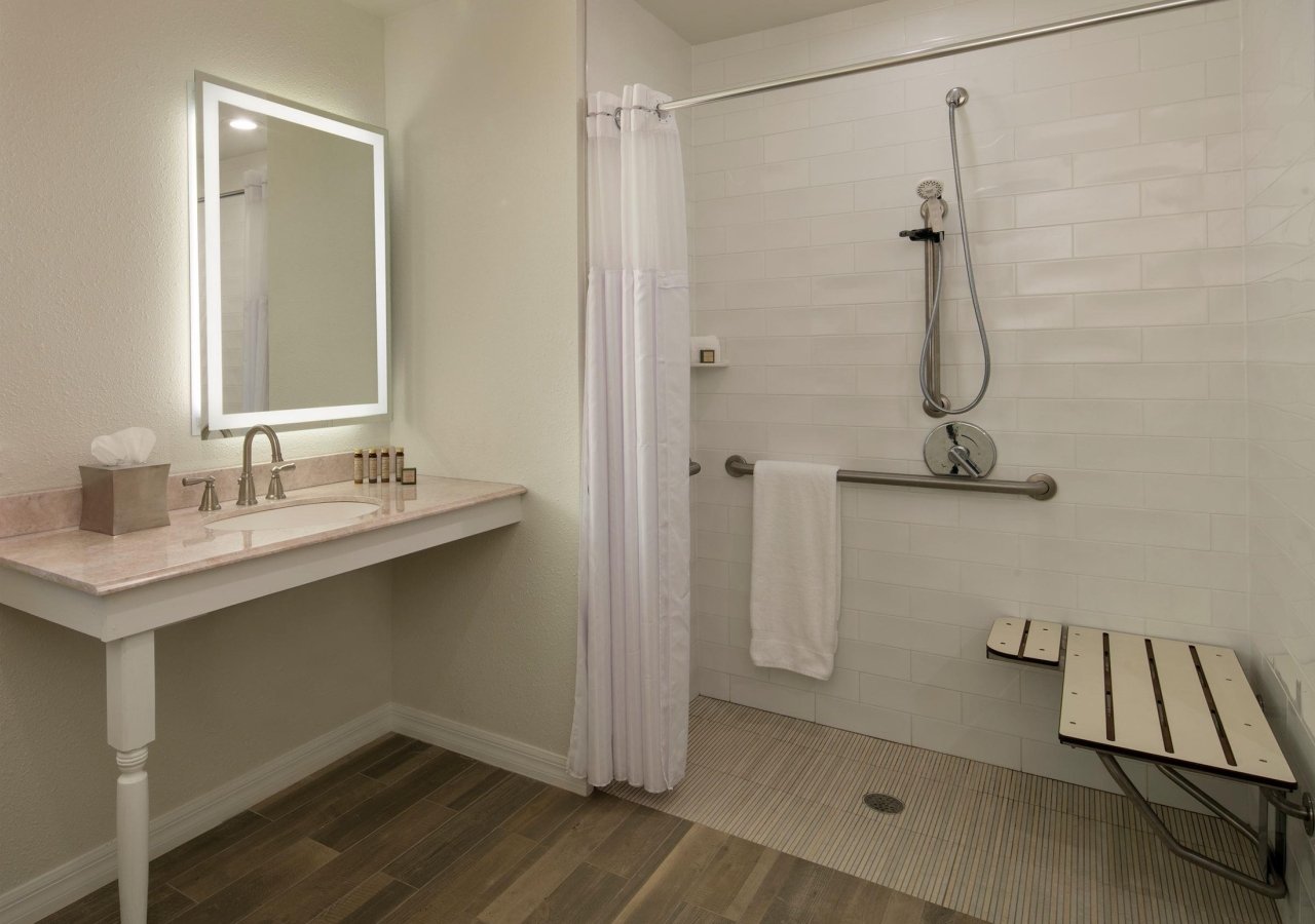 bathroom with wheelchair accessible vanity and shower with bench and grab bars