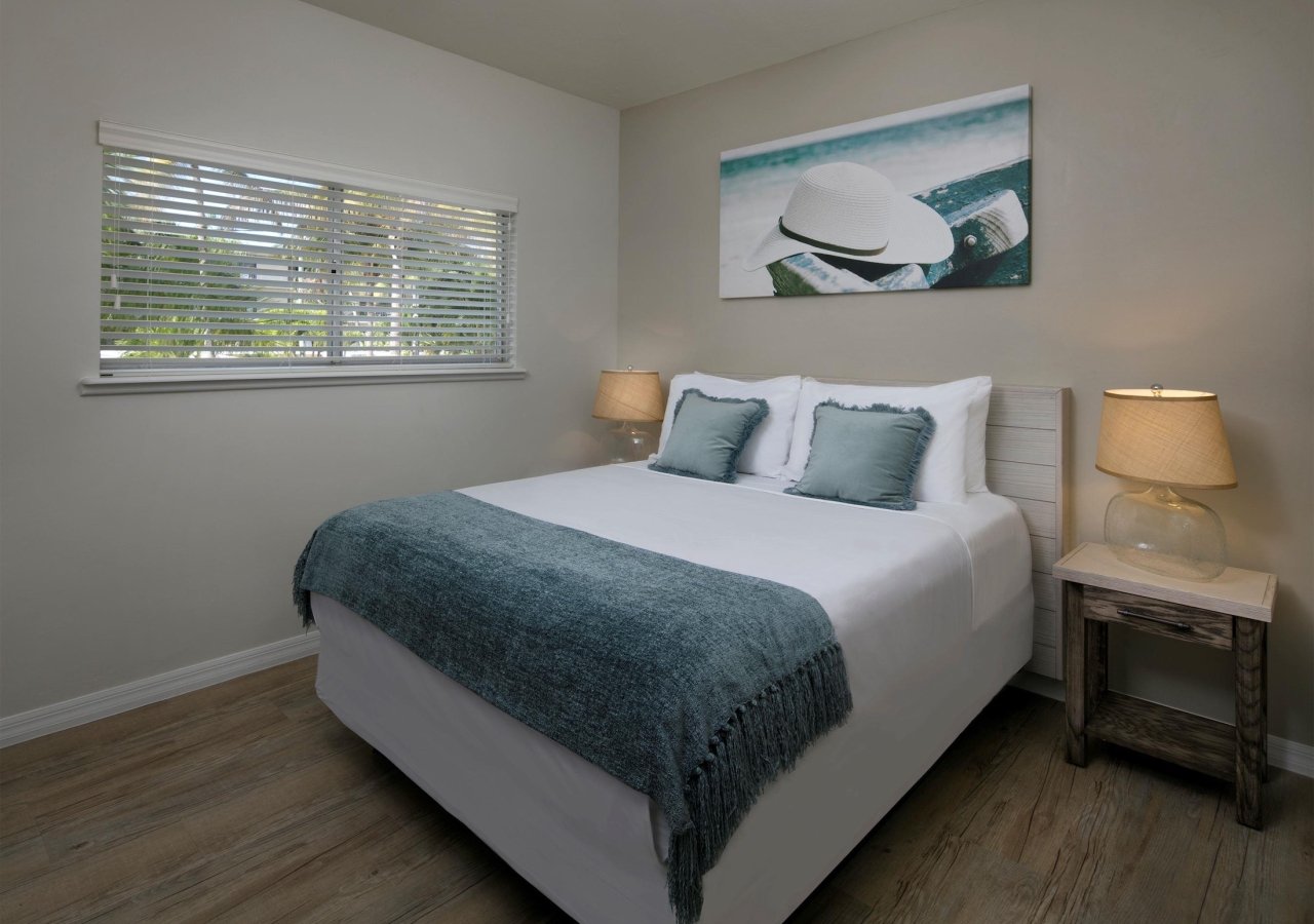 bedroom with queen bed and high window with beach painting on the wall