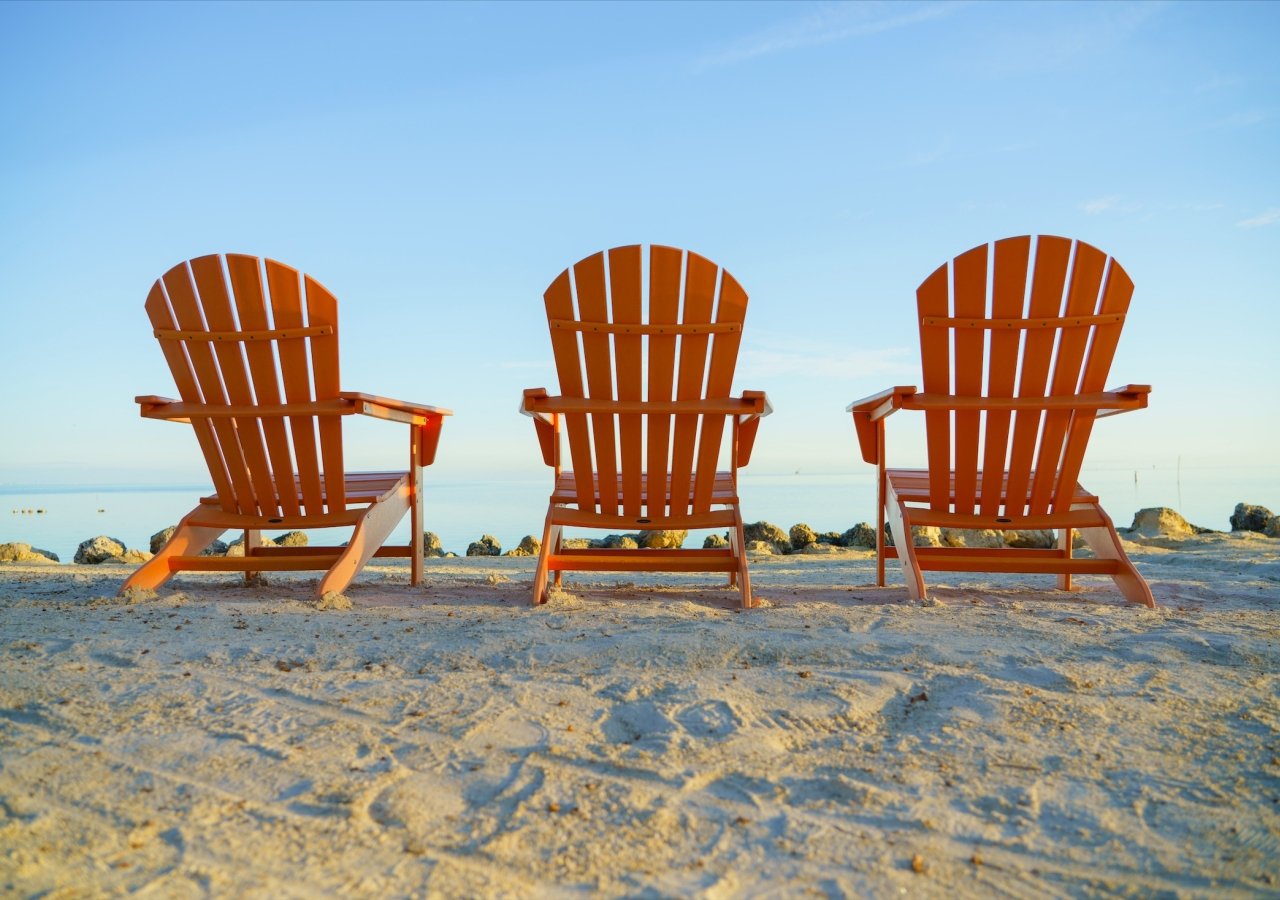 three empty orange beach chairs facing the ocean
