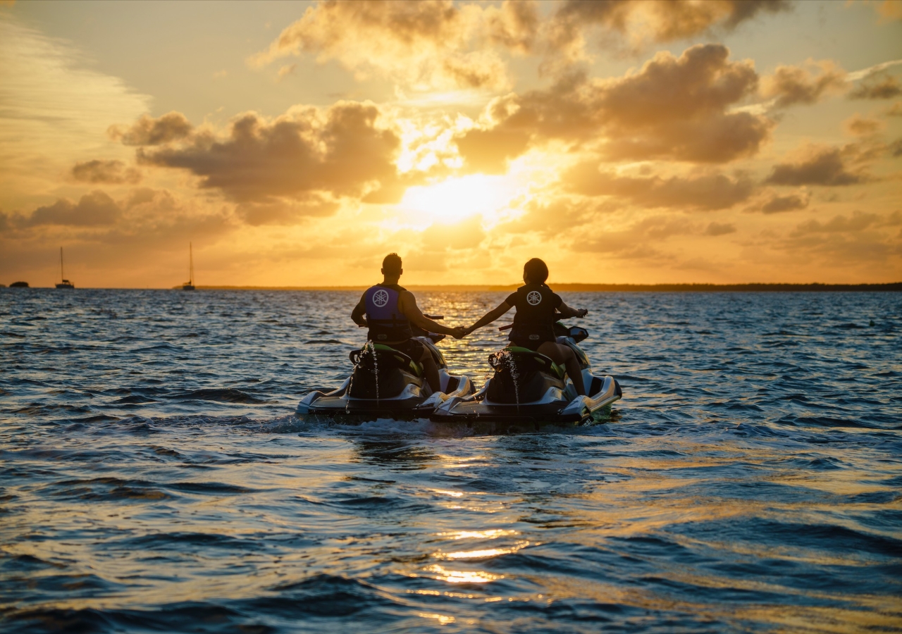couple holding hands on jetskis at sunset
