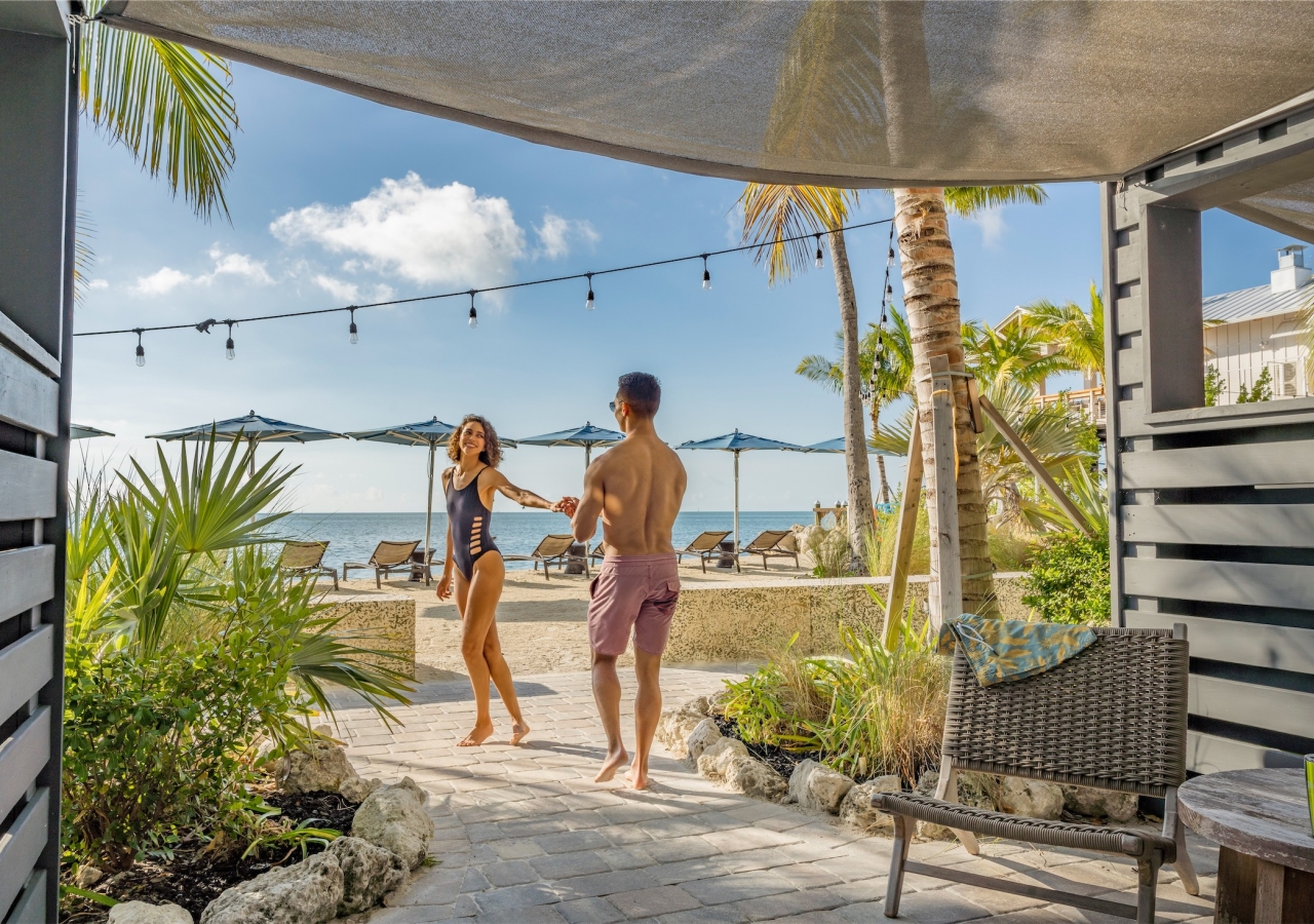 couple holding hands walking to the beach from their lanai