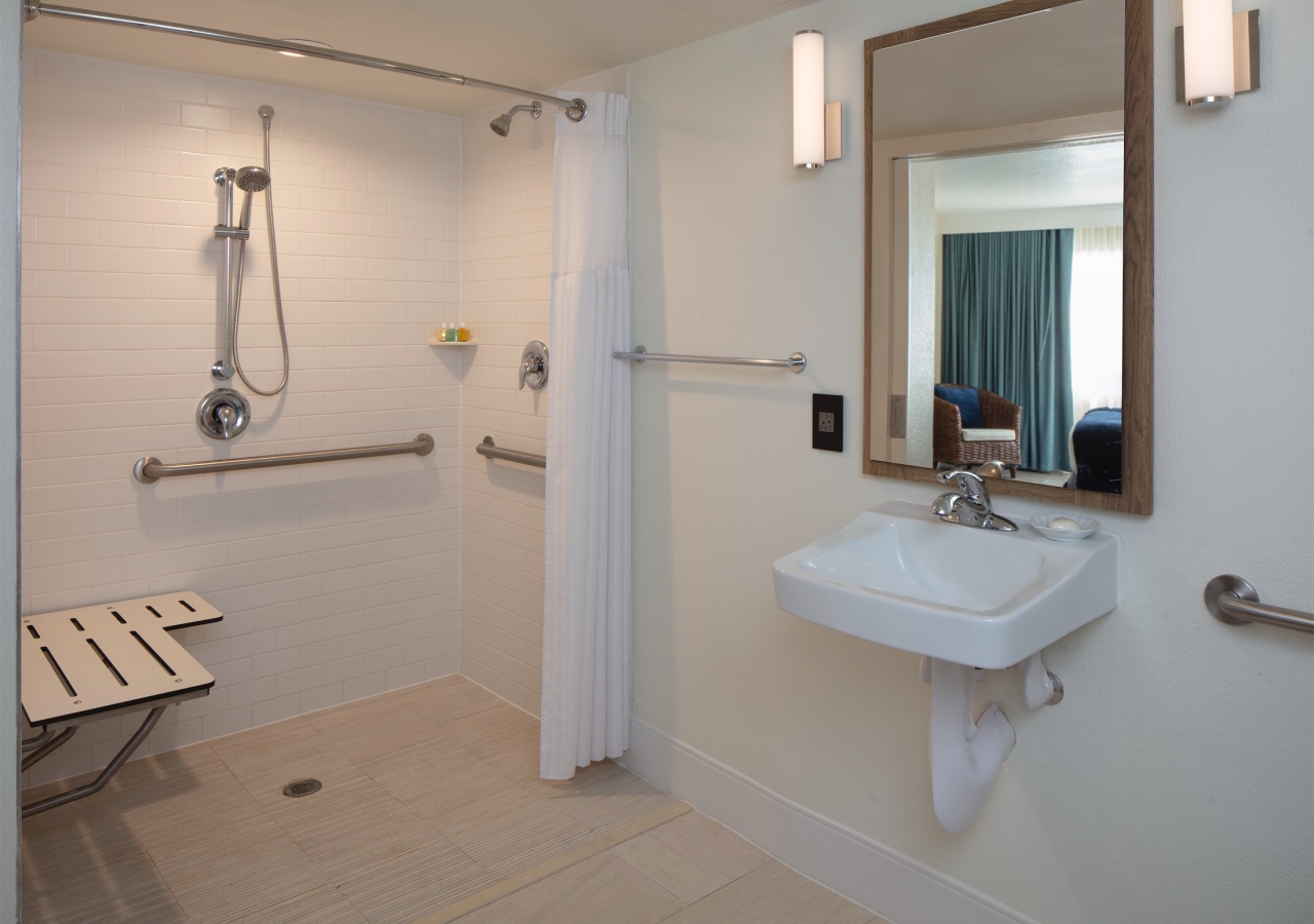 bathroom with wheel-in shower with grab bars and bench