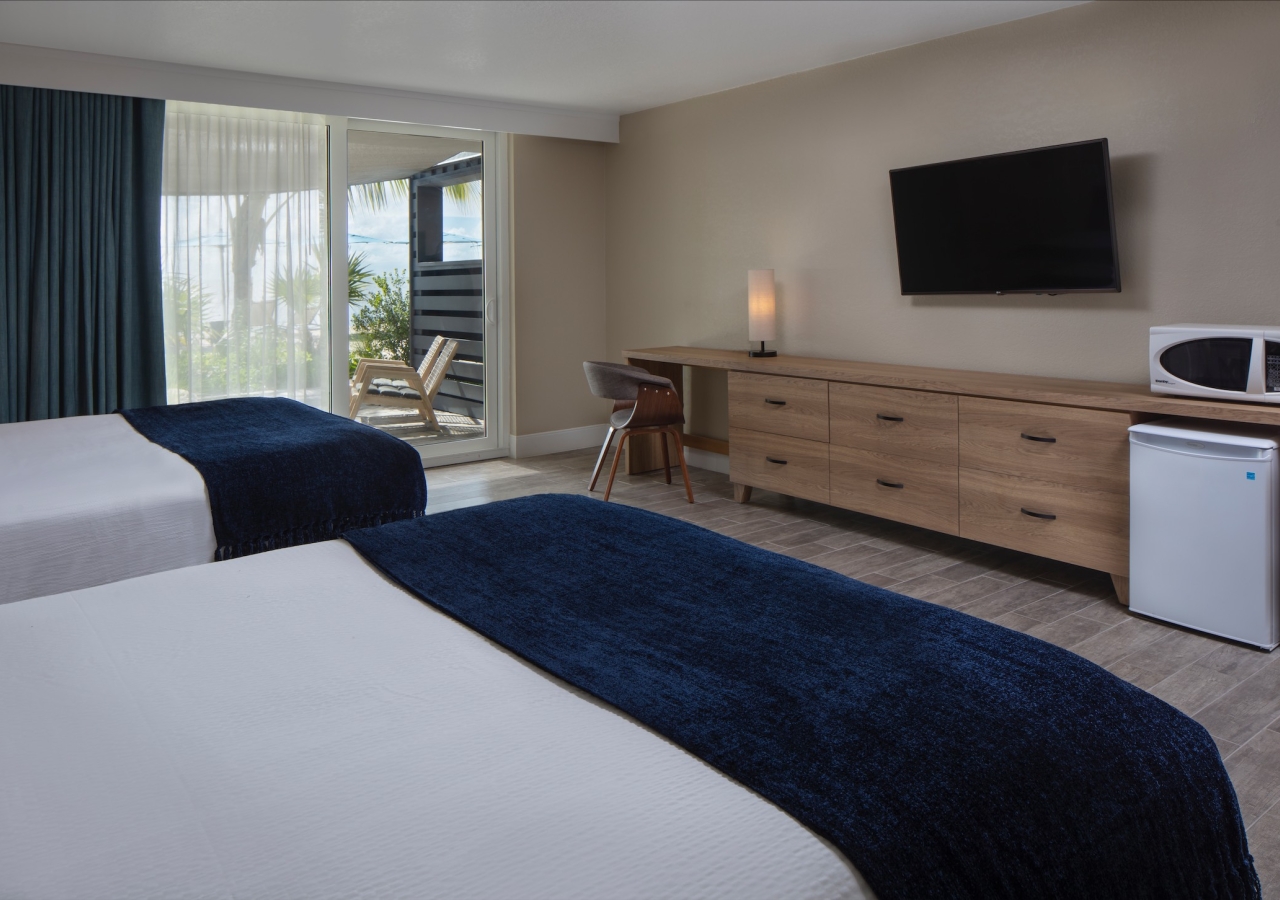 bedroom with two beds and lanai with lounge chairs overlooking the ocean