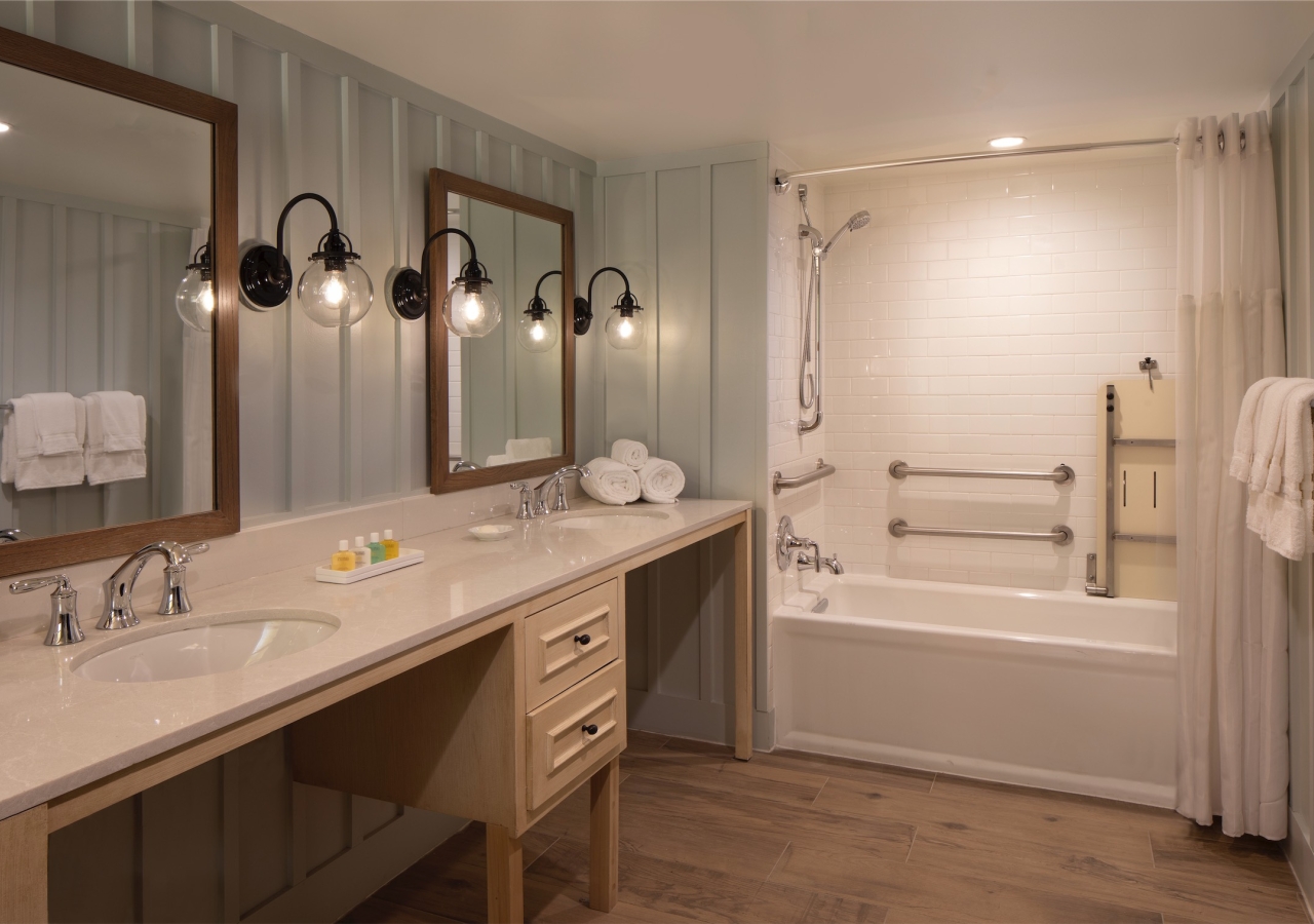 bathroom with twin sinks and a tub with grab bars and bench