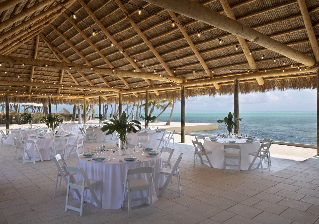 A large tiki set up for a wedding reception with the ocean in the background