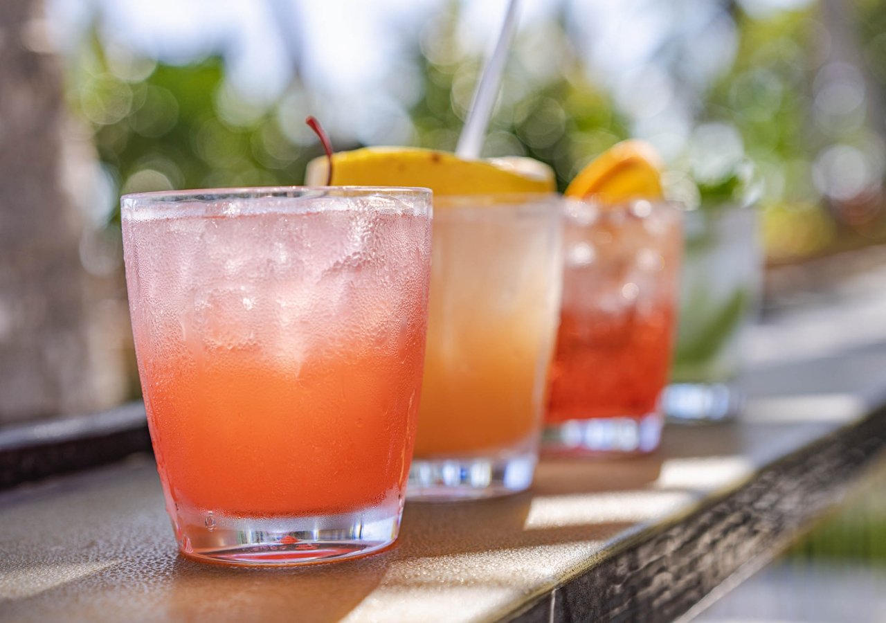 three cocktails on a railing with the ocean in the background