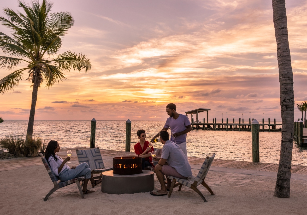 group of friends around a fire pit on the beach at sunset
