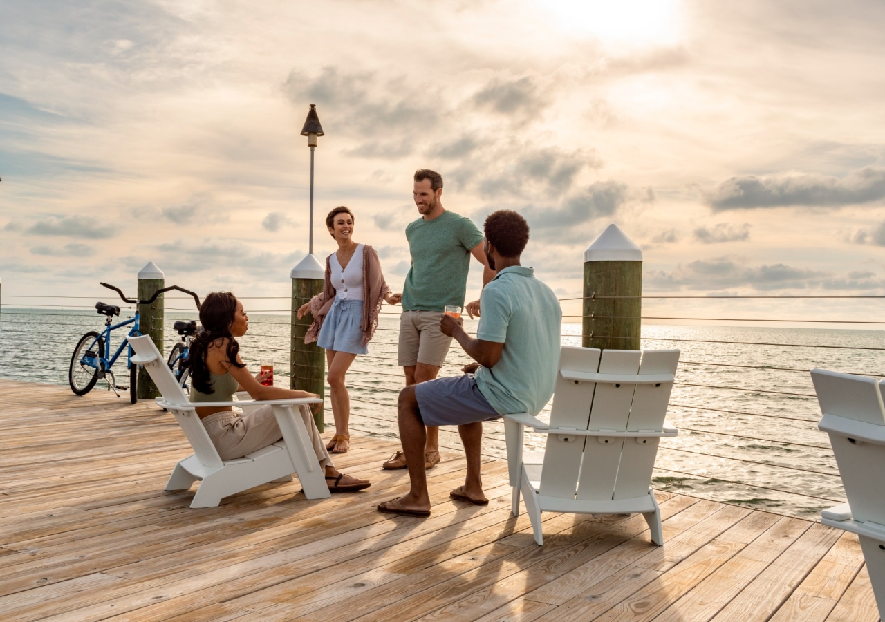 four individuals sitting on chairs on a dock with the ocean in the background