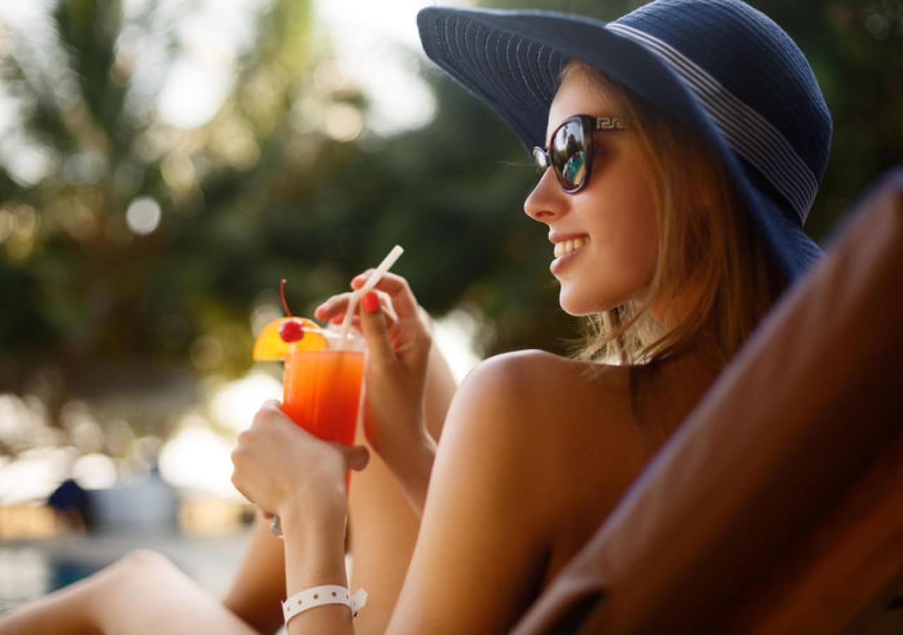 A beautiful woman in a sunhat sipping a refreshing cocktail
