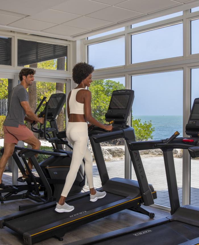 People working out on treadmills with a view of the beach in the background