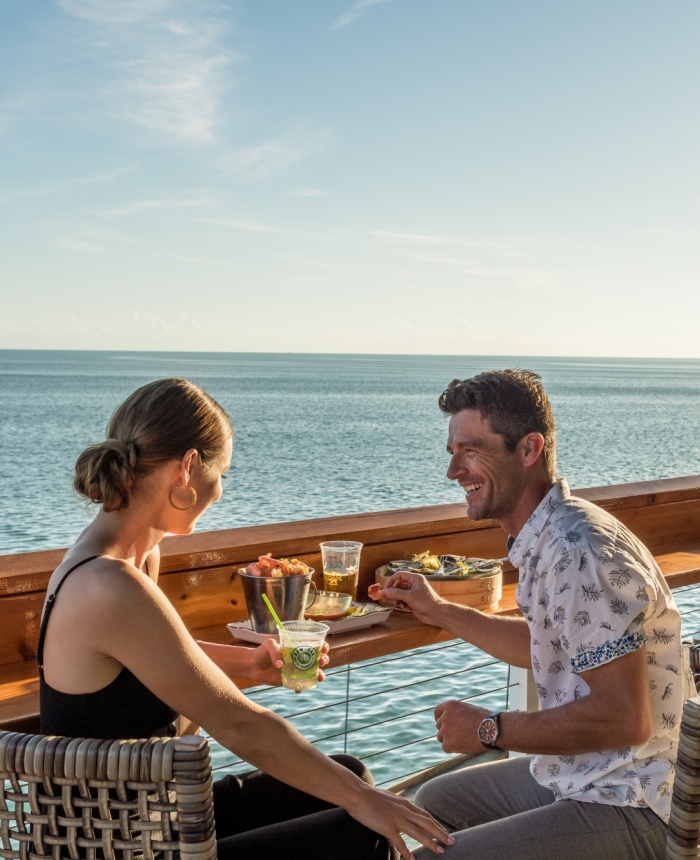Couple enjoying drinks and food at the railing at Raw Bar overlooking the ocean