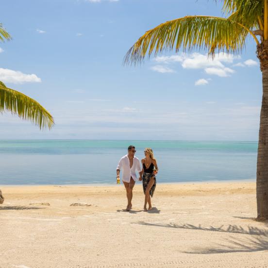 A couple walking on the beach at Three Waters with palm trees surrounding them.