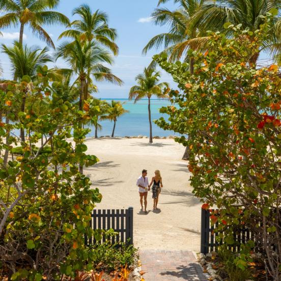 A couple walking on the beach at Three Waters with palm trees surrounding them.