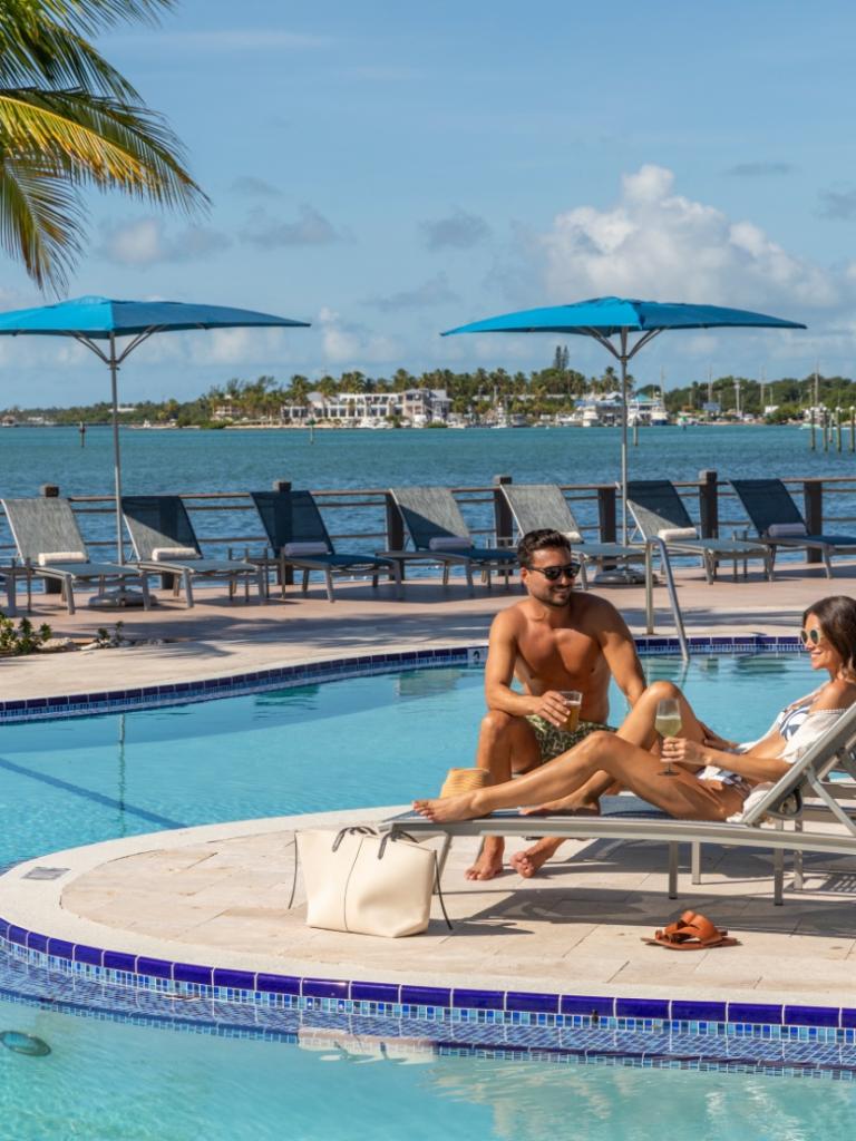 A couple sitting by the pool on chaise lounges.