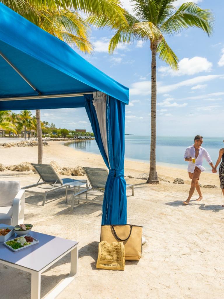A couple walking on the beach next to a cabana.