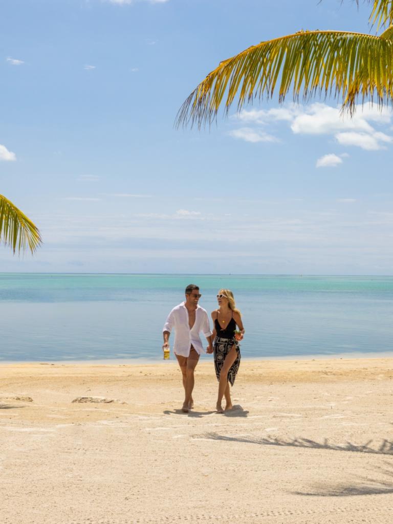 A couple walking on the beach at Three Waters with palm trees surrounding them.