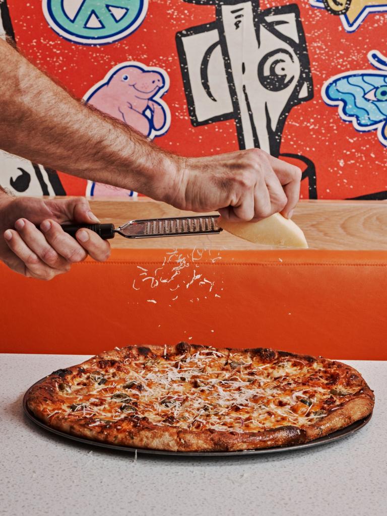 A fresh pizza with parmesan being sprinkled over it.
