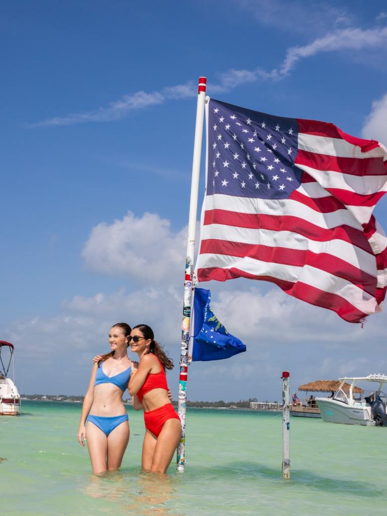 Two girls standing in the water at the Islamorada Sand Bar with an American Flag behind them.