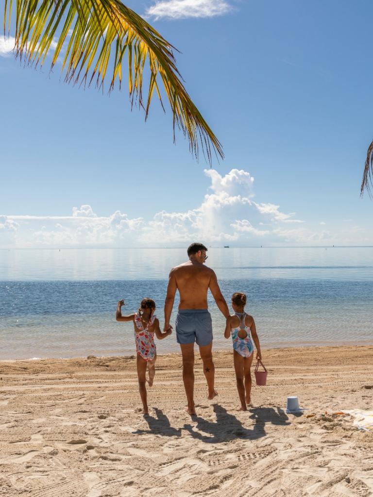 A dad walking to the ocean with his two girls at a beach at Three Waters Resort & Marina in Islamorada, Florida.