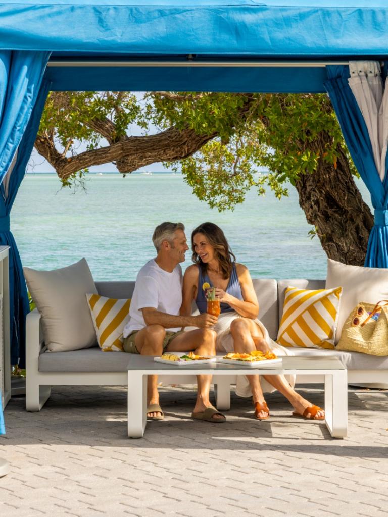 A couple is sitting under a cabana by the ocean.