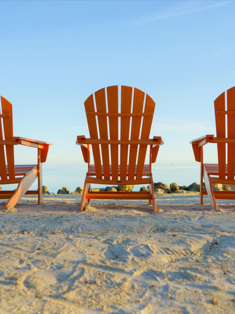 three empty orange beach chairs facing the ocean