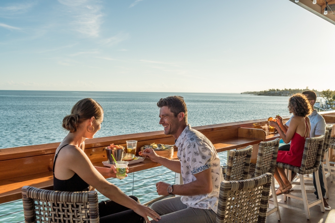Couple enjoying drinks and food at the railing at Raw Bar overlooking the ocean