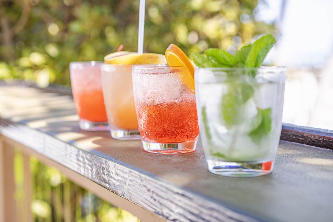 four cocktails on a railing with the ocean in the background